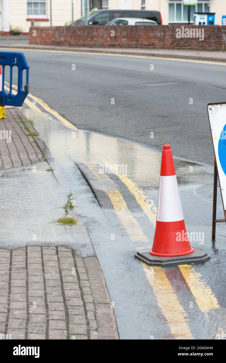 Water flows from a burst water main pipe under a road - note the bulging road surface June 2021 UK Stock Photo