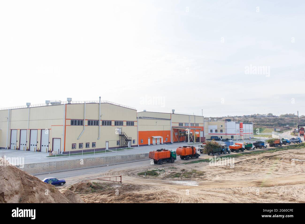 Queue with garbage trucks and tractors near warehouse of waste. Dump of