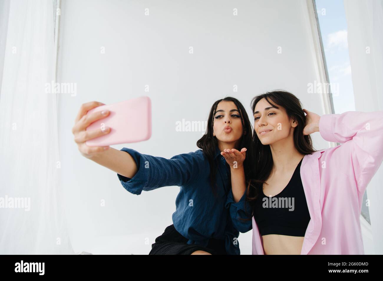 young armenian woman sending air kiss while taking selfie on smartphone with friend Stock Photo