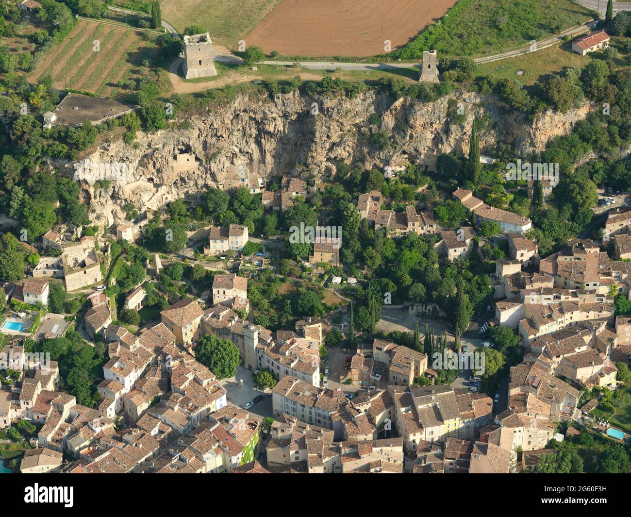 AERIAL VIEW. Two medieval towers standing at a clifftop above an old village and some cliff dwellings. Cotignac. Var, France. Stock Photo