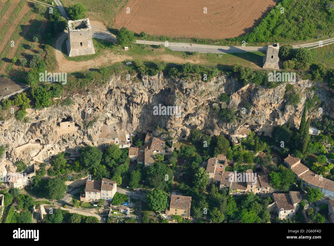 AERIAL VIEW. Two medieval towers standing at a clifftop above an old village and some cliff dwellings. Cotignac. Var, France. Stock Photo
