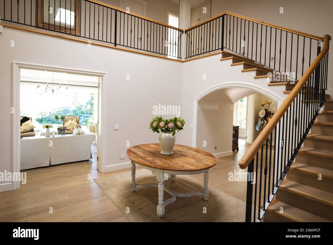 General view of house interior with table and vase with flowers in spacious hallway and staircase Stock Photo