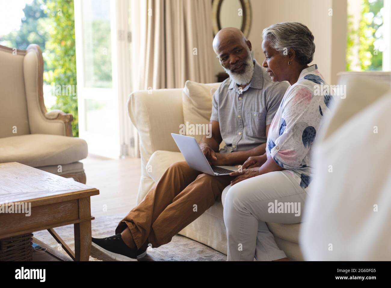 Senior african american couple sitting on sofa using laptop and talking ...