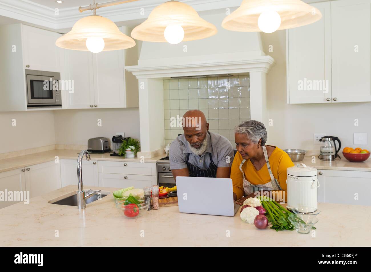 Senior african american couple cooking together in kitchen using laptop ...