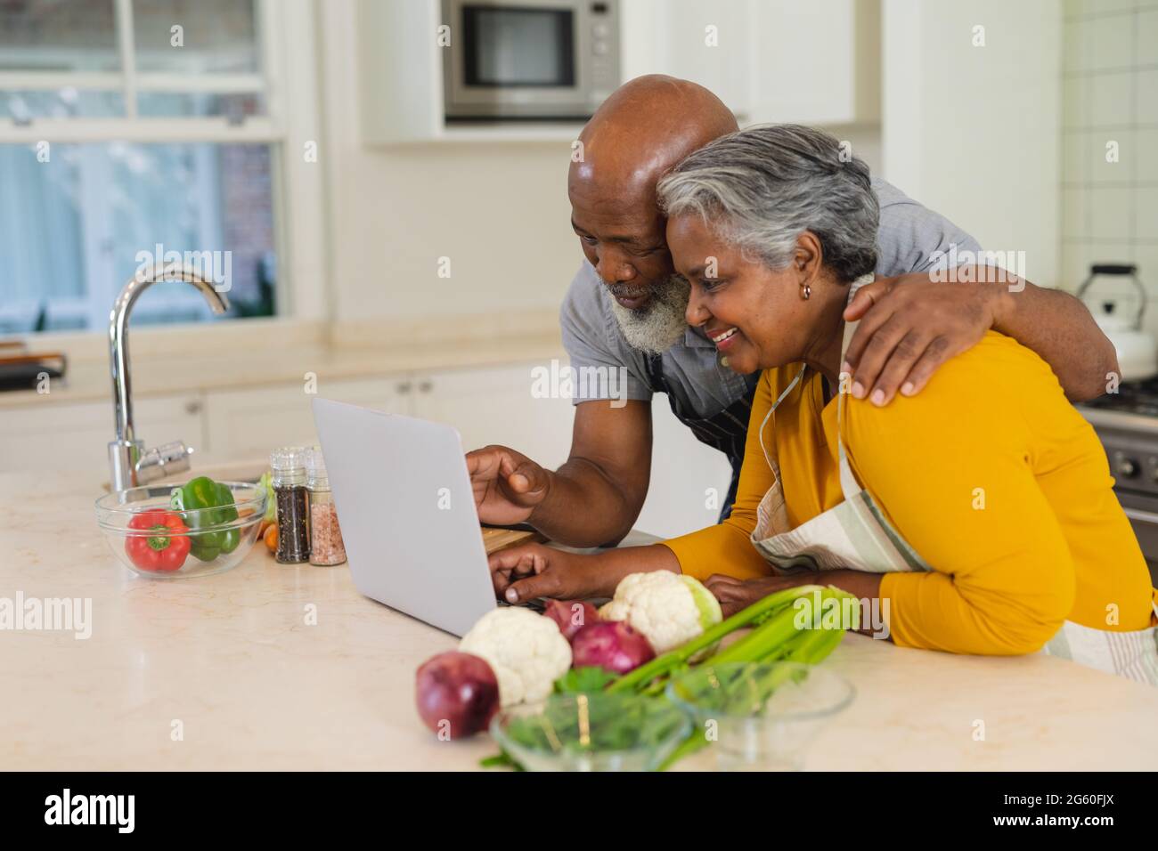 Senior african american couple cooking together in kitchen using laptop ...