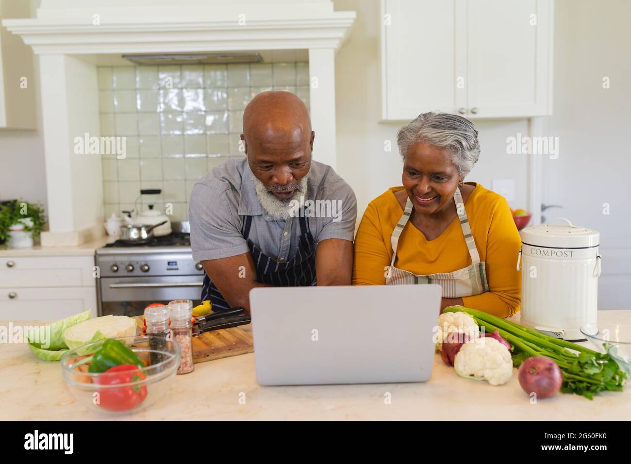 Senior african american couple cooking together in kitchen using laptop ...
