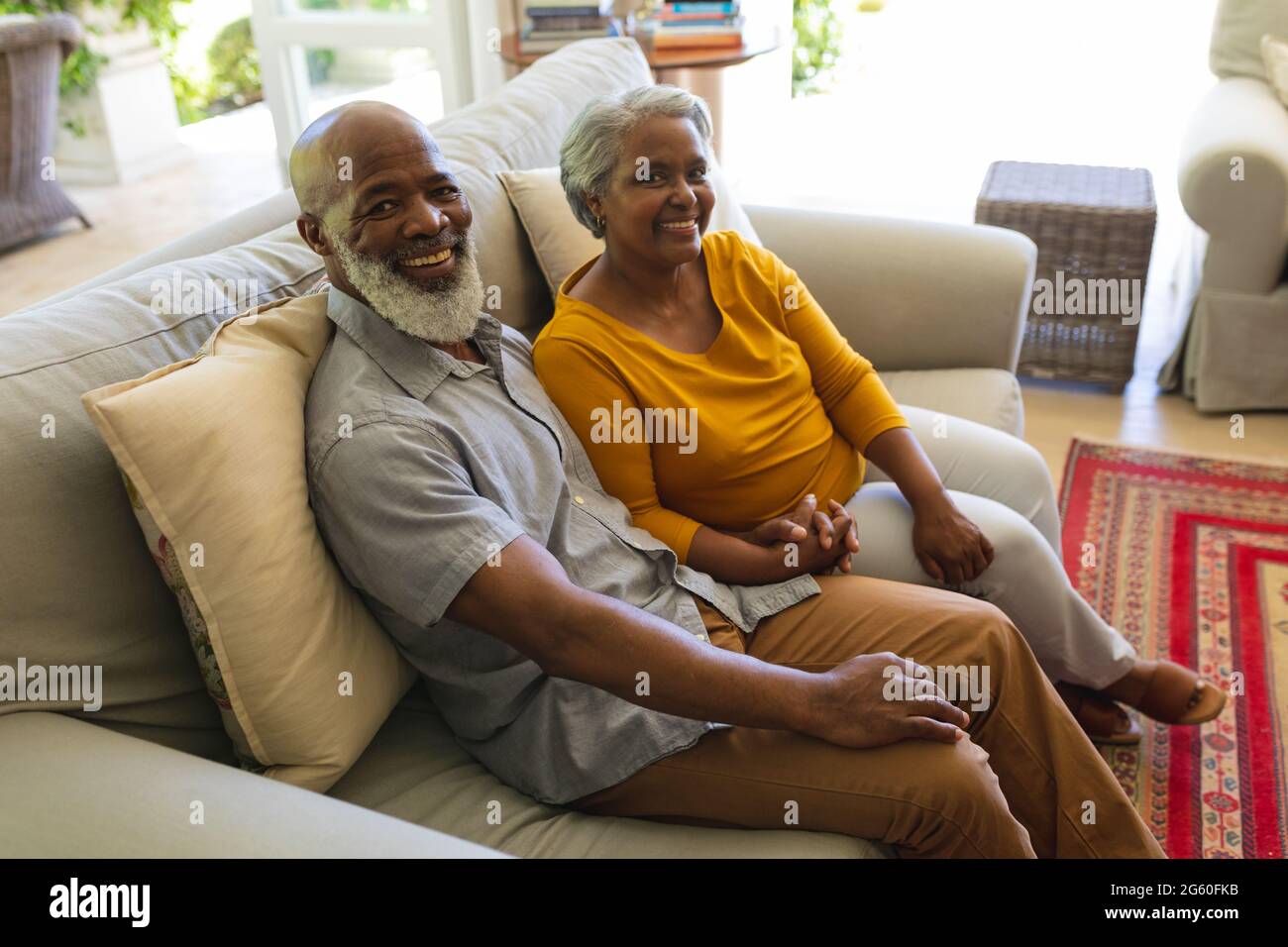 Portrait of senior african american couple sitting on sofa holding ...
