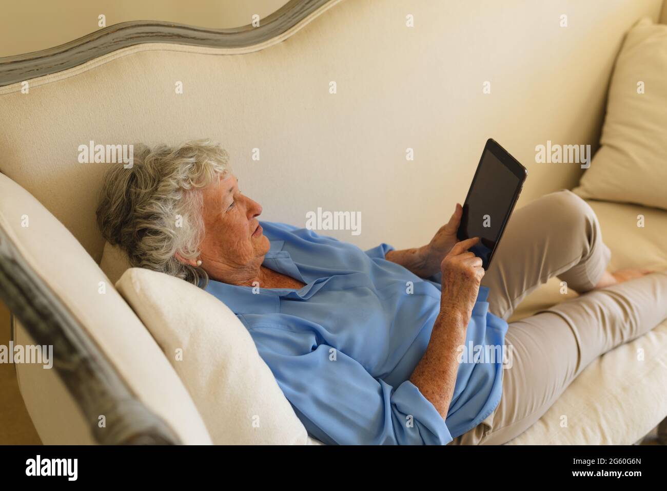 Senior caucasian woman lying on sofa and using tablet Stock Photo