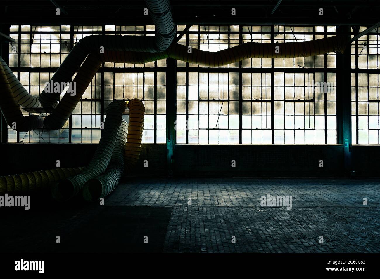 Dirty old factory windows with brick floor and ductwork Stock Photo