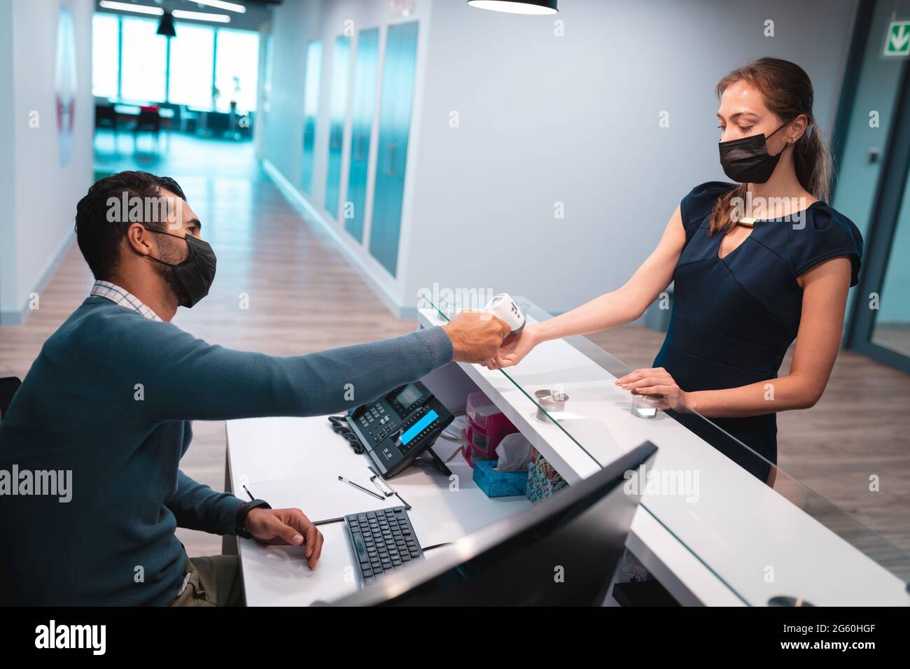 Two diverse businesspeople wearing face masks and taking temperature at reception Stock Photo