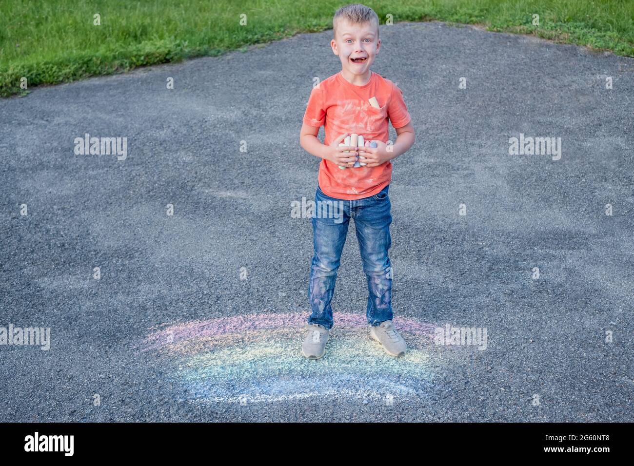 Surprised boy holding colored chalk in his hand, standing on a rainbow school playground.The concept of cleaning stains on clothes. High quality photo Stock Photo