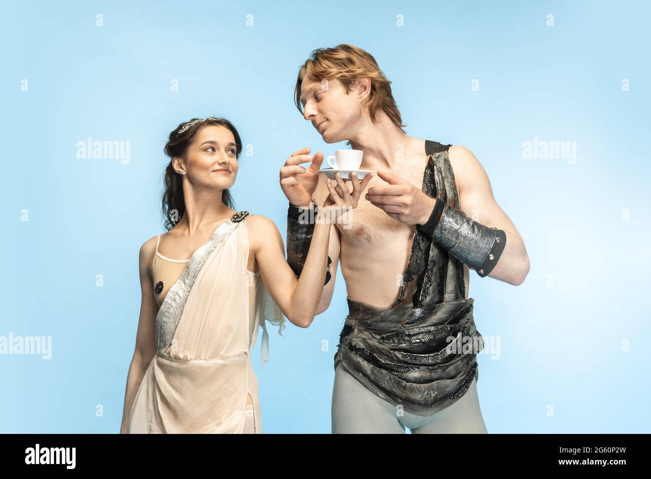 Coffee time. Young couple of ballet dancers in ancient Rome costums at blue studio. Stock Photo