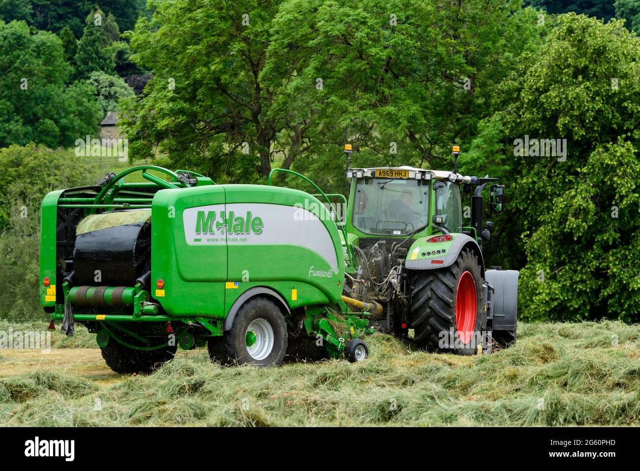Hay or silage making (farmer in farm tractor at work in rural field, collecting dry grass, round bale being wrapped in baler) - Yorkshire England, UK. Stock Photo
