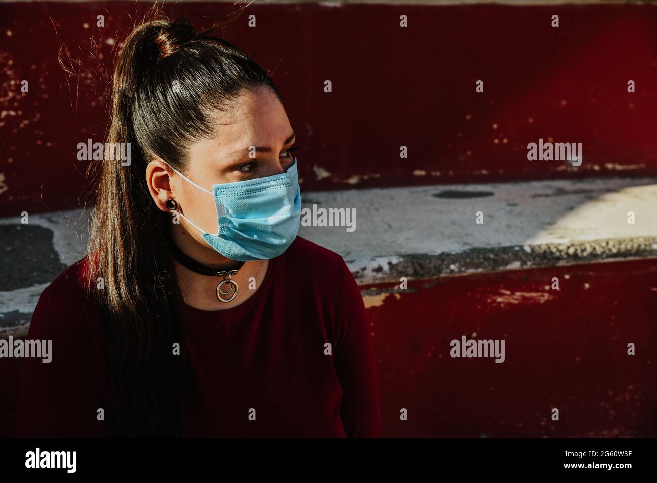Caucasian female wearing a facemask on red background - pandemic concept Stock Photo