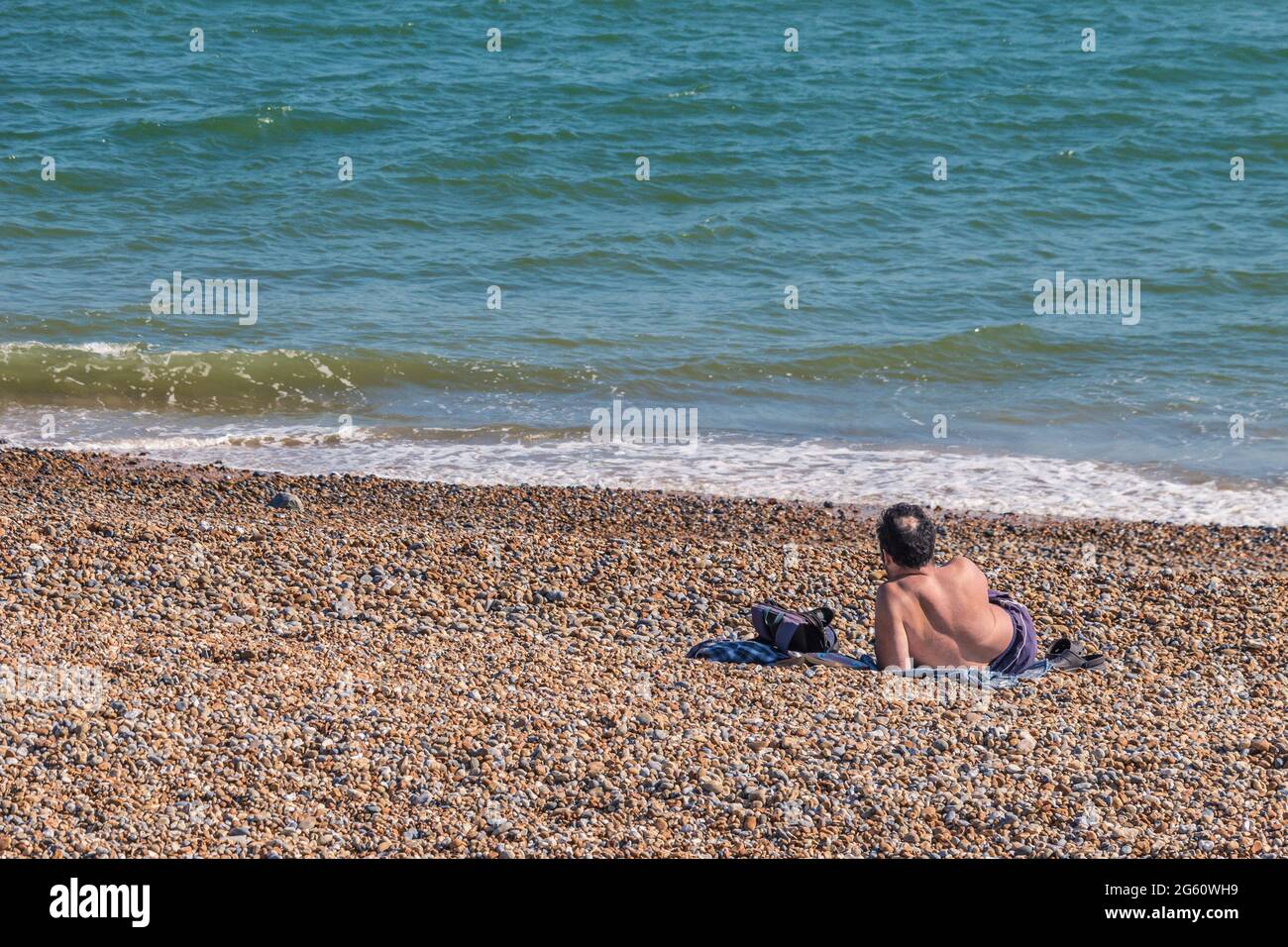 One man sitting on the beach on a hot day in Hastings, UK Stock Photo