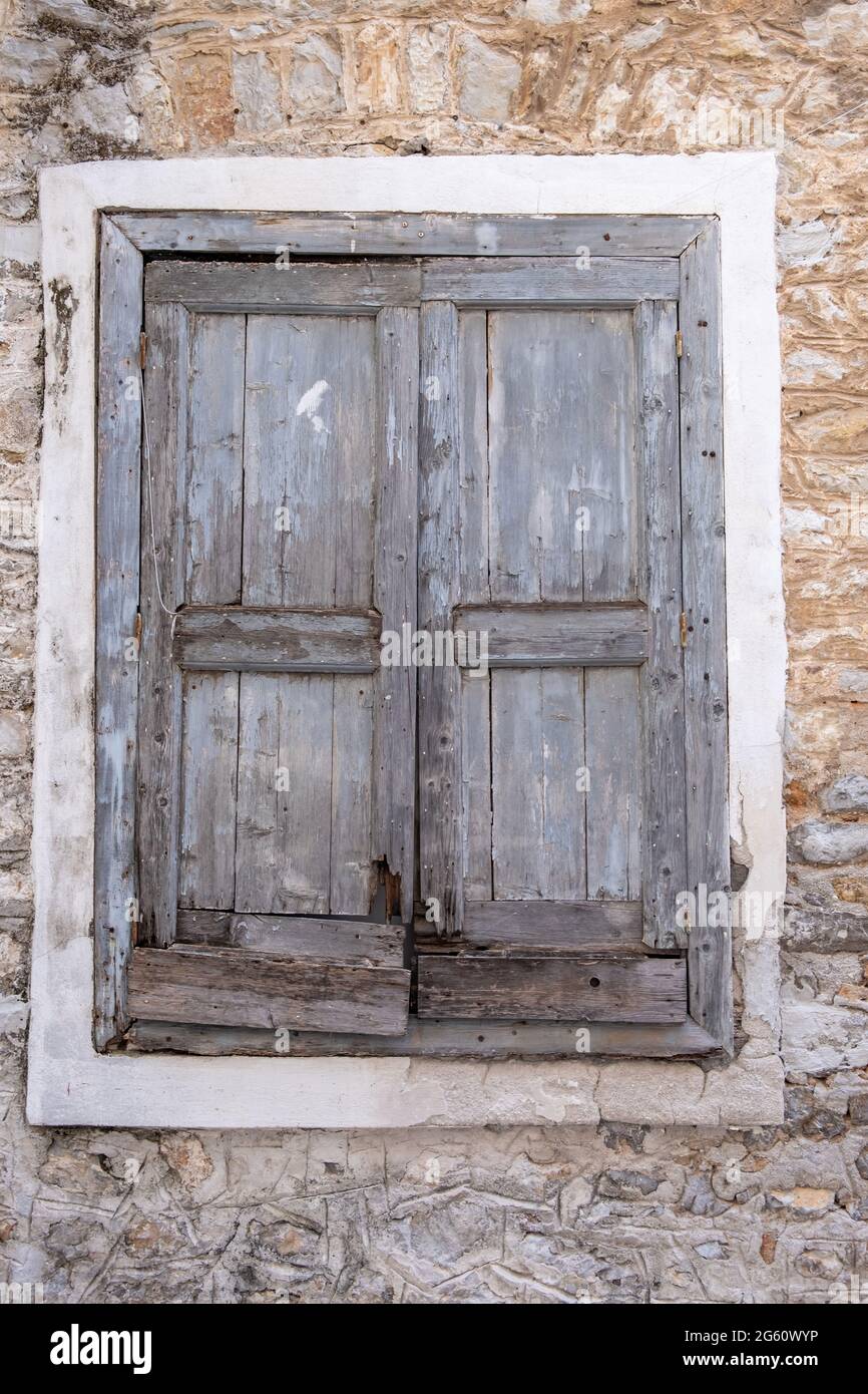 Old window wooden shutters closed, stone wall building facade. Abandoned house at Naflion old town, Greece. Vertical view. Stock Photo