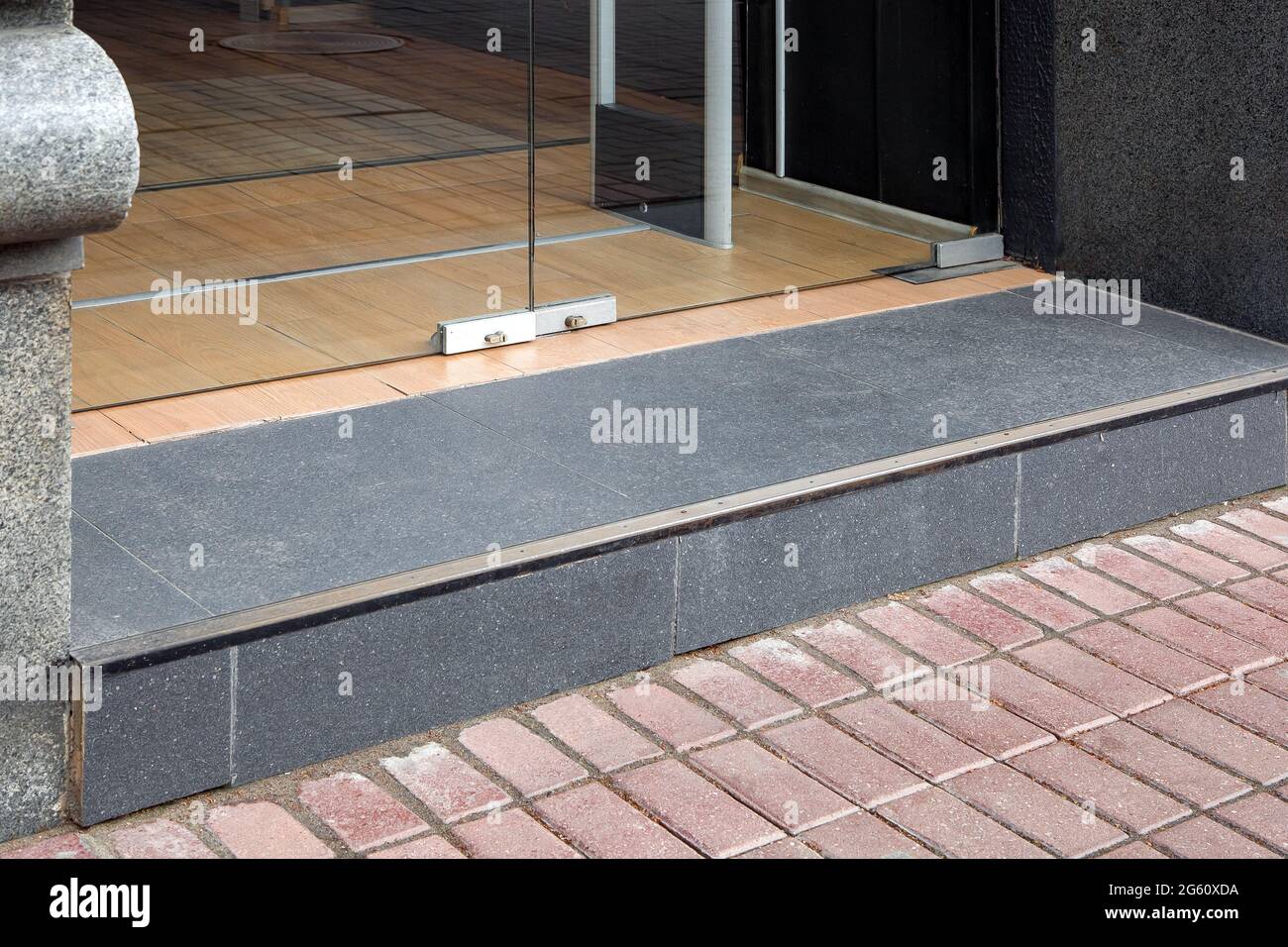 a threshold with a doorstep at the entrance to the store with a tempered glass door in the doorway tiled with dark gray granite tiles side view, nobod Stock Photo