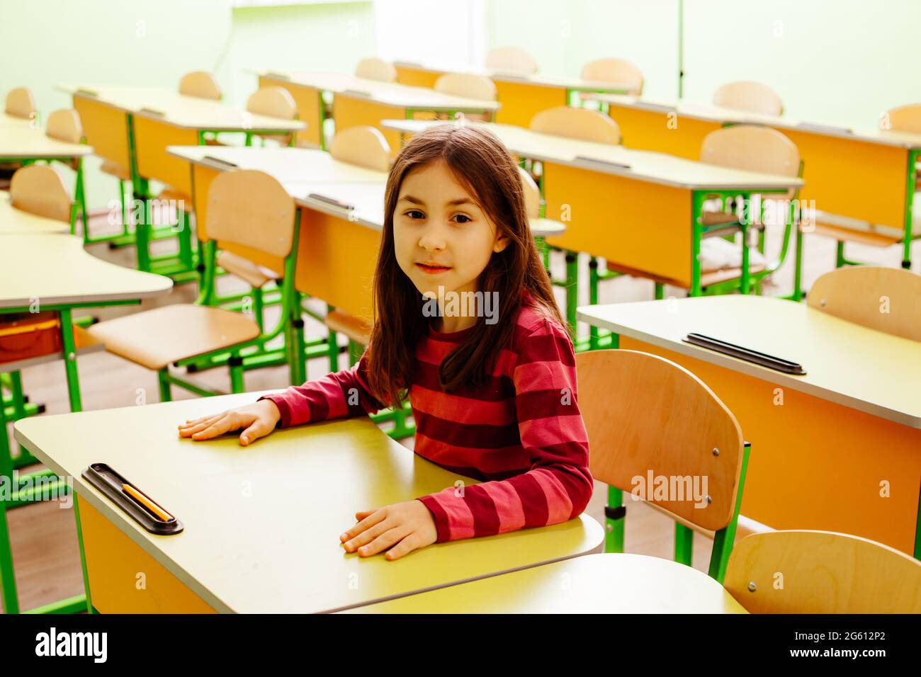 The joyful schoolgirl is sitting at a desk in the classroom Stock Photo ...