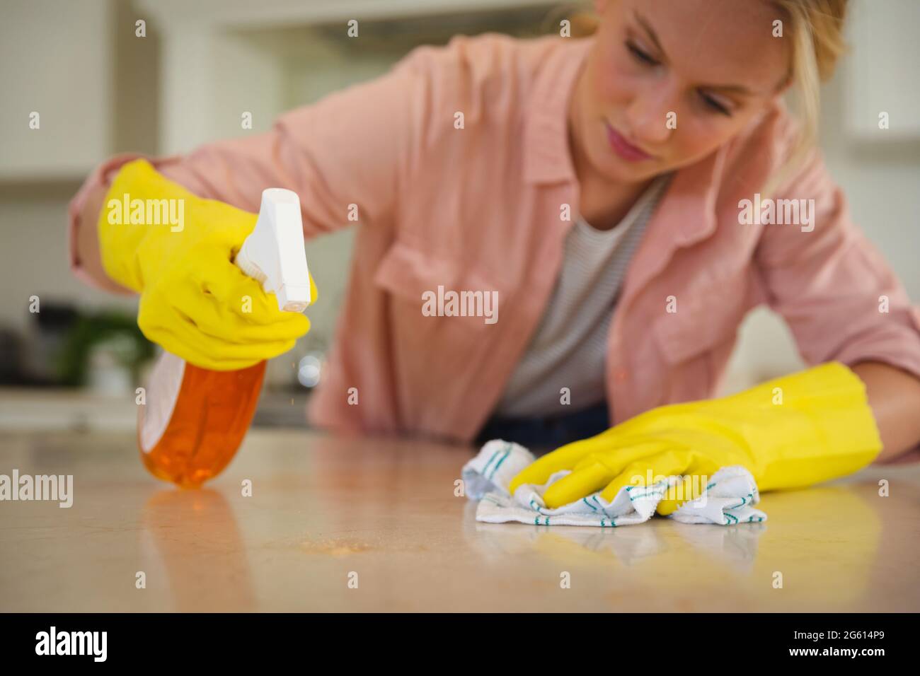 Caucasian woman wearing rubber gloves cleaning kitchen worktop with cloth and spray Stock Photo