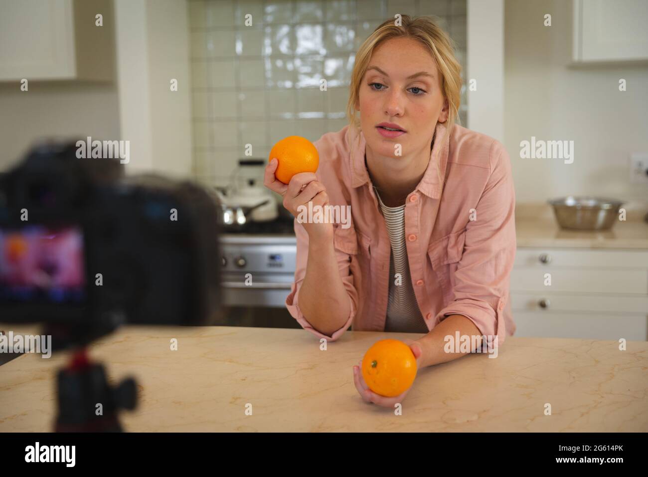 Caucasian woman in kitchen holding oranges and talking to camera, making cooking vlog Stock Photo