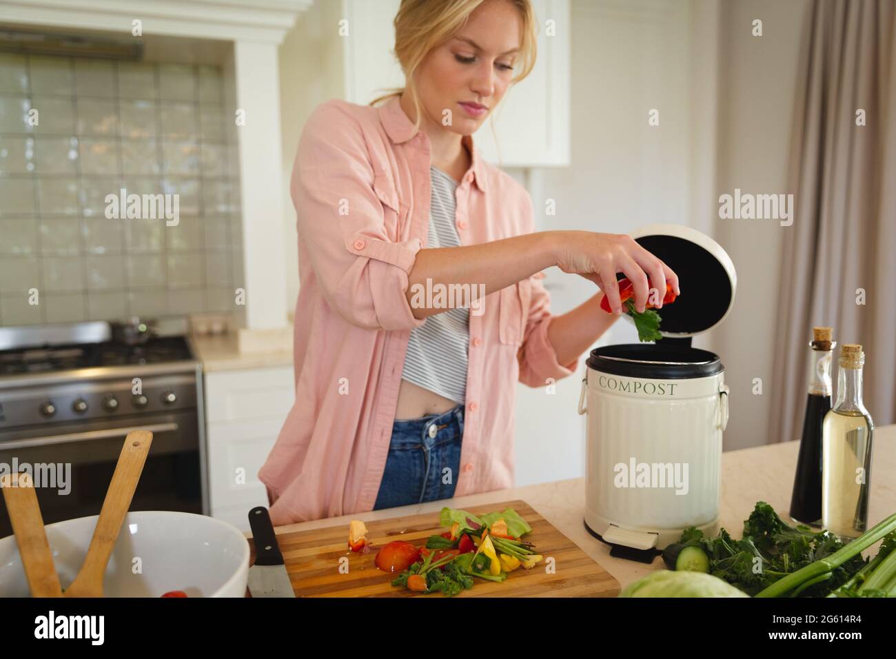 Caucasian woman standing in kitchen preparing food, composting vegetable waste Stock Photo