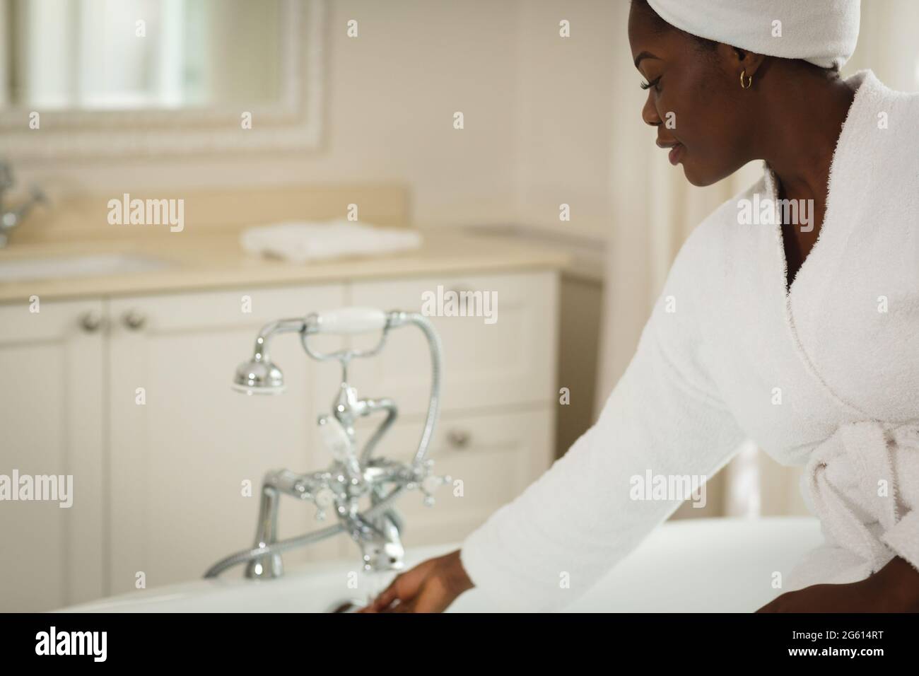 African american woman sitting in bathroom wearing bathrobe, running bath Stock Photo Alamy
