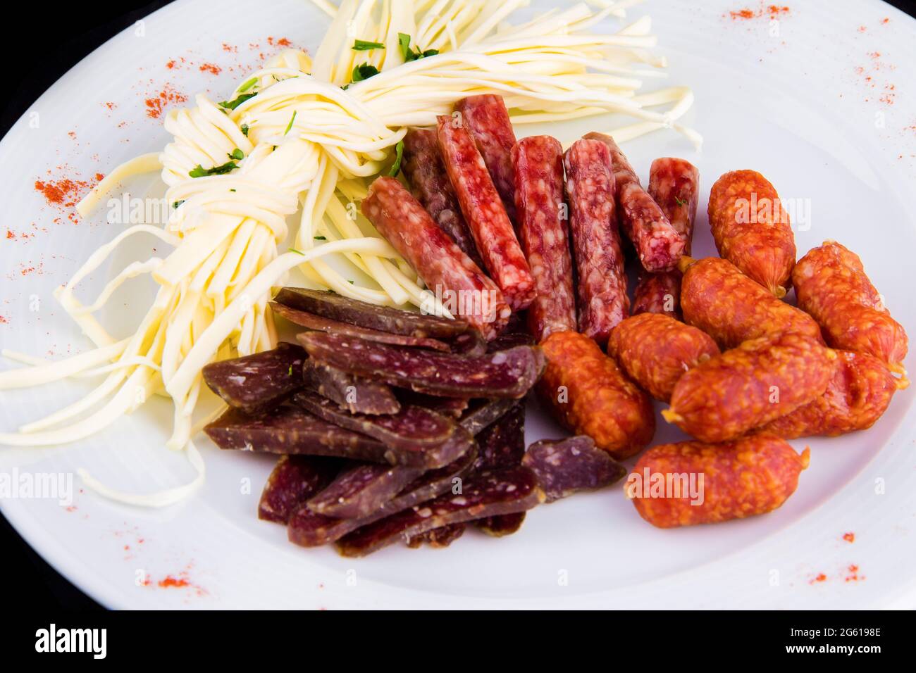 Beer appetizer: cecil cheese, picolini sausages, sujuk, jorki. Plate with delicious sliced smoked sausages, close up isolated on black background Stock Photo