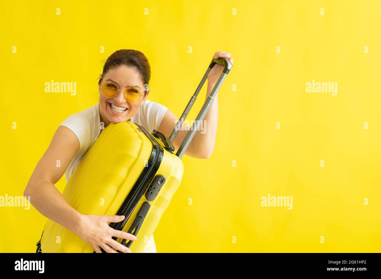 Beautiful caucasian woman fooling around with a suitcase on a yellow background. A charming girl imitates playing the guitar. The joy of the journey Stock Photo