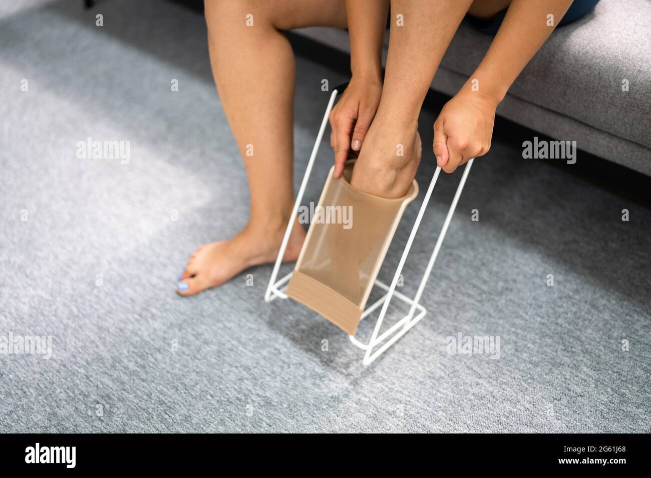 Woman Putting On Medical Compression Stockings Using Stocking Aid Puller Stock Photo