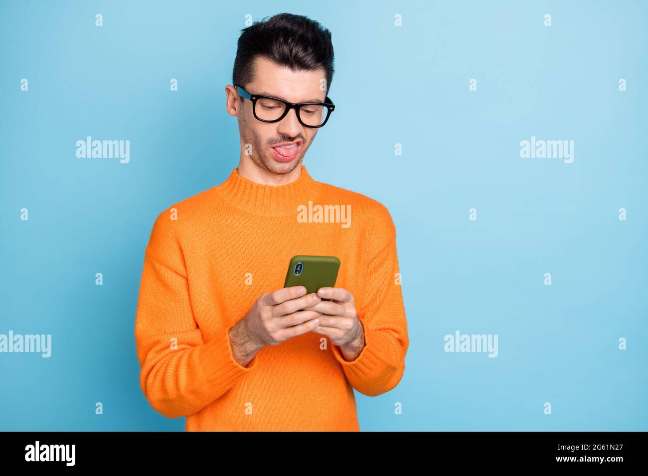 Portrait of young weirdo guy hold phone tongue out displeased eyewear isolated on blue color background Stock Photo