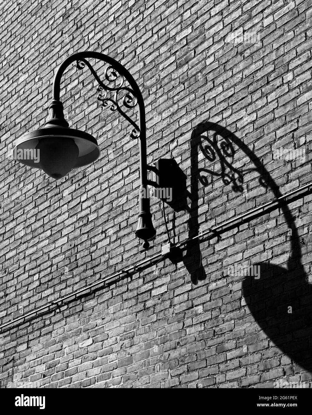 An overhead outdoor lighting fixture and its shadow on a brick wall. Stock Photo