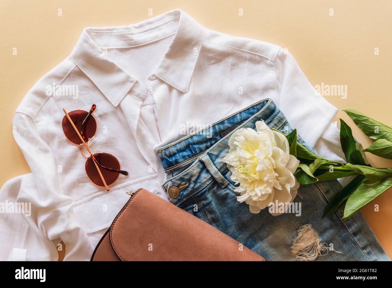 Feminine summer fashion flat lay with blouse, handbag, sunglasses and white peony flower on beige background. Stylish summer clothes, beauty concept. Stock Photo