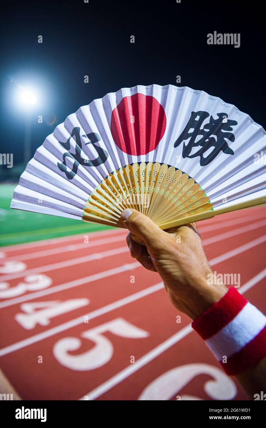 Hand of Japanese sports athlete standing outdoors holding a fan decorated with kanji characters spelling out hisshō, certain victory in English Stock Photo