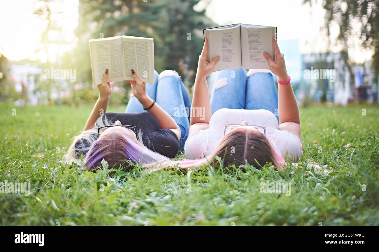 Teenagers reading books together in a university campus while lying in grass - Millennials learning and preparing to exam - Recreation and culture con Stock Photo