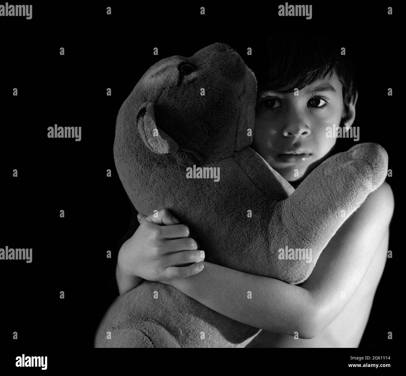 child with a sweet look hugging a stuffed tiger with black background, monochrome horizontal copy space Stock Photo