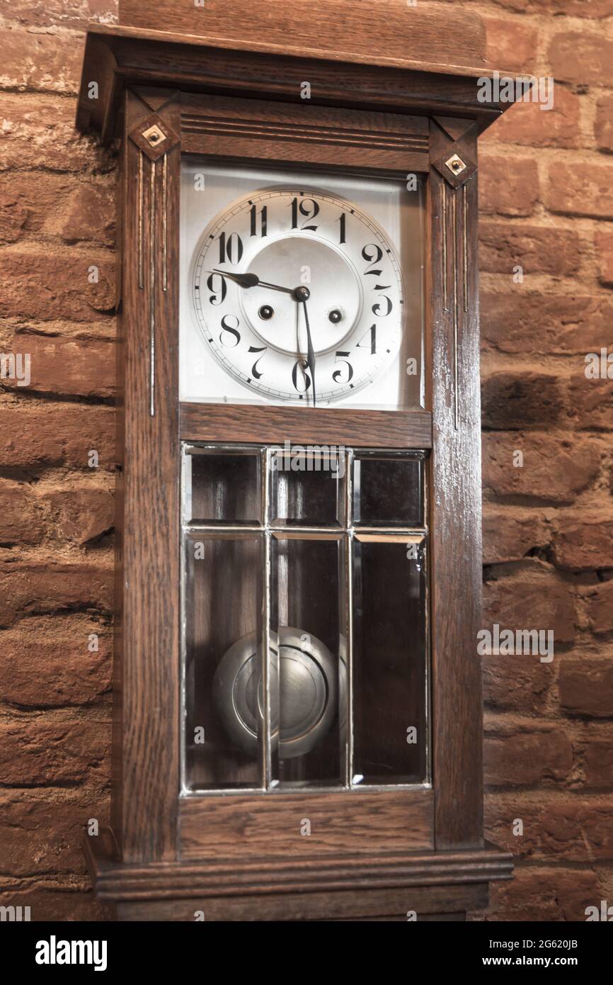 Vintage grandfather clock in wooden body stands near red brick wall. Close up vertical photo Stock Photo