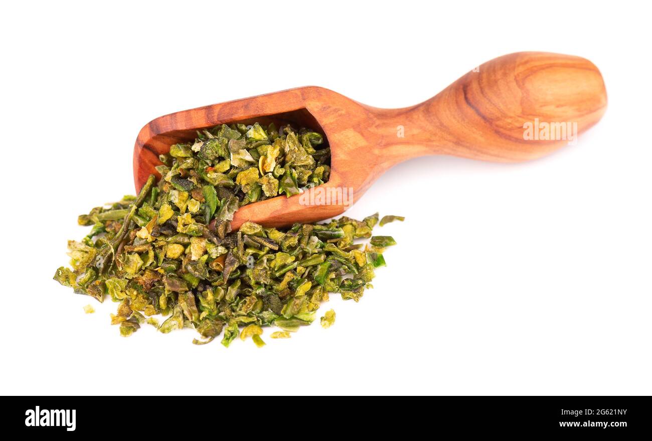 Dried green paprika flakes with seeds in olive scoop, isolated on white