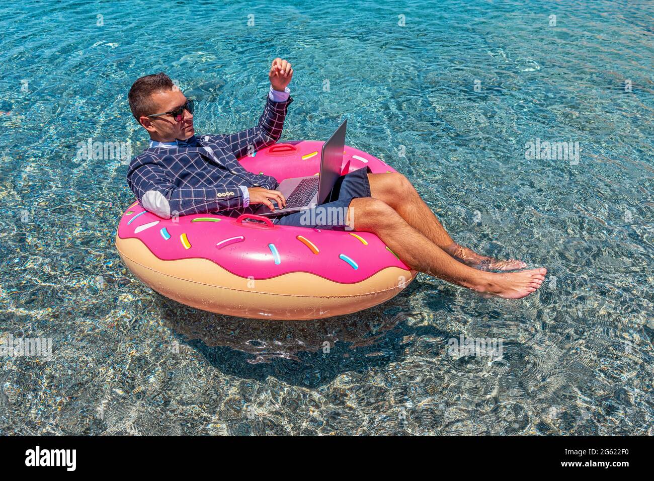 Businessman using laptop computer on an inflatable donut in the sea ...