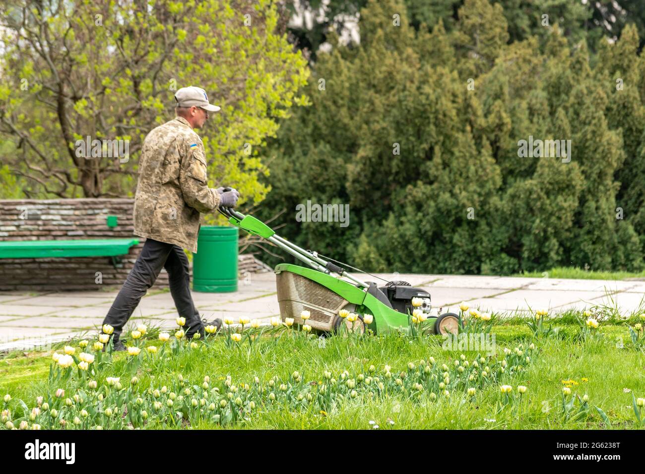 Kiev, Ukraine - April 27, 2021: A man with a lawn mower mows the grass in the park. Stock Photo