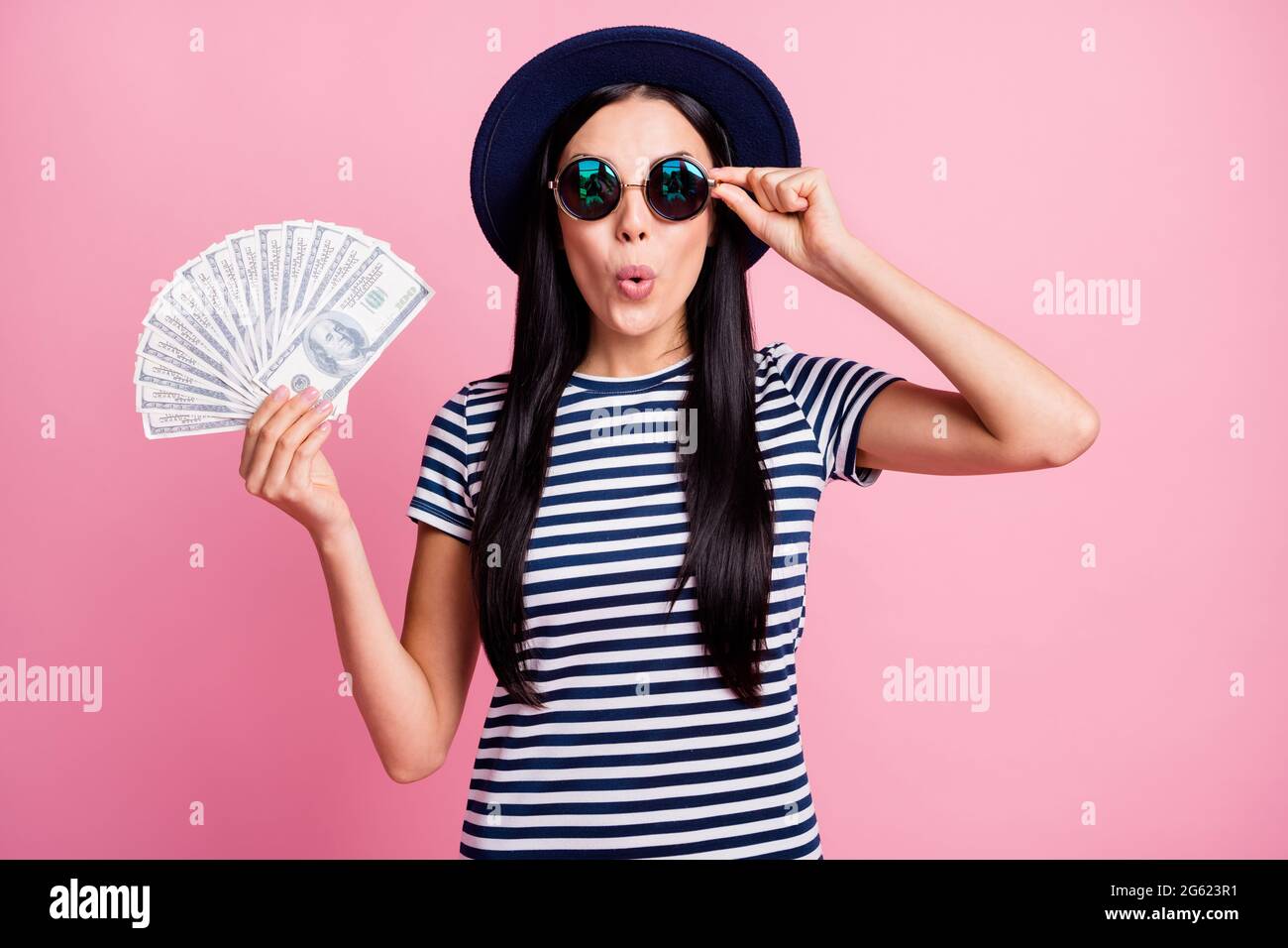 Photo portrait of shocked girl holding cash fan in one hand touching glasses isolated on pastel pink colored background Stock Photo