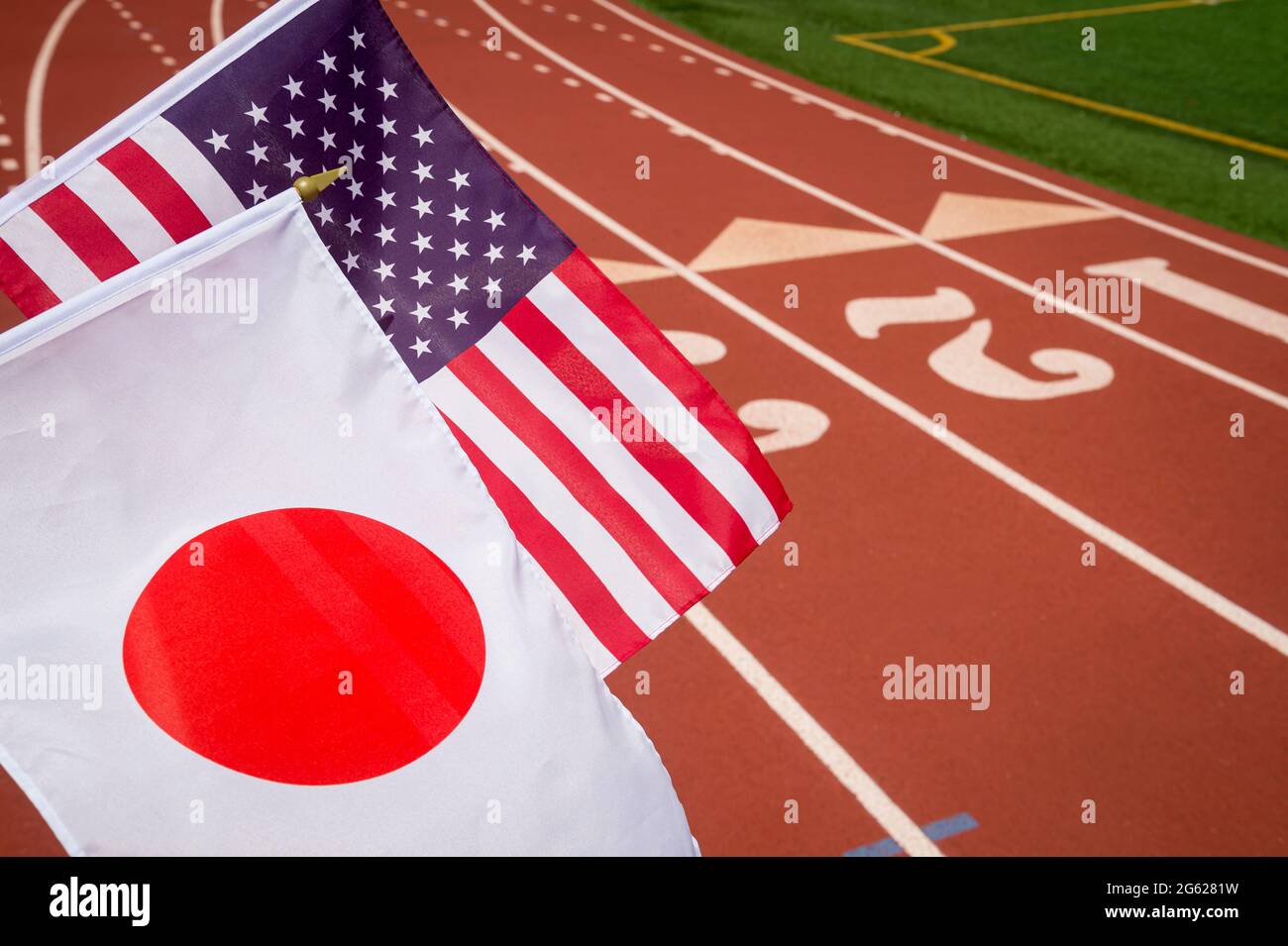 Bright sunny view of USA and Japanese flags flying together in front of the numbered lanes at the starting line of a red running track Stock Photo