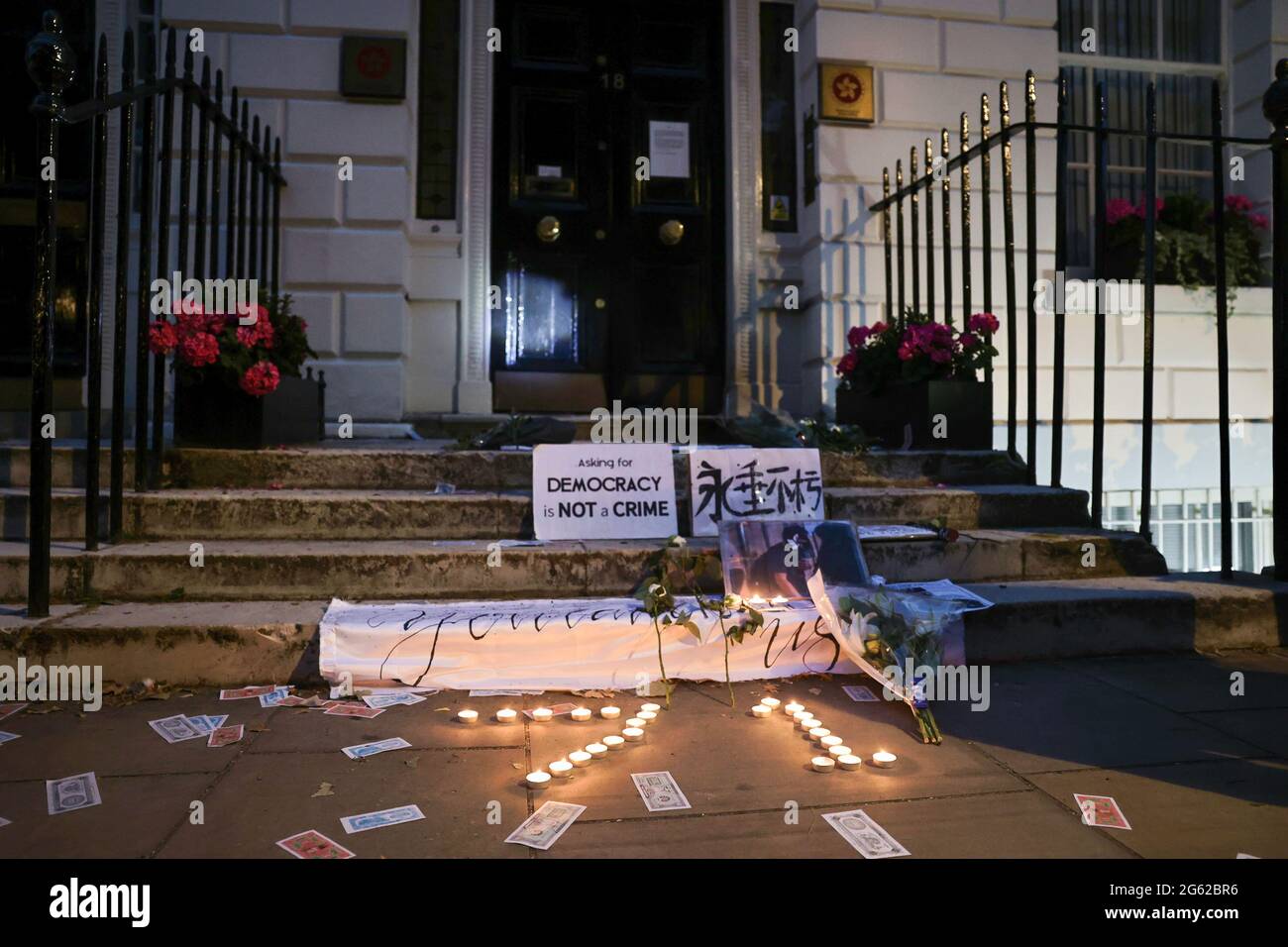 Protesters leave flowers and lit candles in front of the Hong Kong Economic and Trade Office to mourn the death of a Hongkonger during the demonstration. Hongkongers held demonstrations in ten different cities in the UK to protest against the one year anniversary of the promulgation of the Hong Kong National Security Law and the Centennial anniversary of the Chinese Communist Party. In London, participants gathered outside the Chinese Embassy and marched to Chinatown where the main event took place. The crowds later moved to the Hong Kong Economic and Trade Office and set smoky flares outside Stock Photo