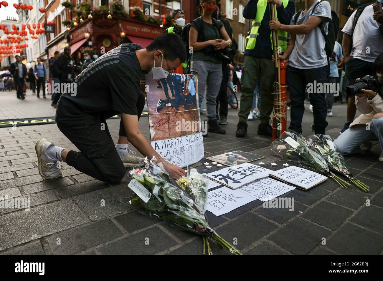 A protester places flowers and placards to mourn the death of a Hongkonger during the demonstration. Hongkongers held demonstrations in ten different cities in the UK to protest against the one year anniversary of the promulgation of the Hong Kong National Security Law and the Centennial anniversary of the Chinese Communist Party. In London, participants gathered outside the Chinese Embassy and marched to Chinatown where the main event took place. The crowds later moved to the Hong Kong Economic and Trade Office and set smoky flares outside as a symbolic sign of cursing the Hong Kong Governmen Stock Photo