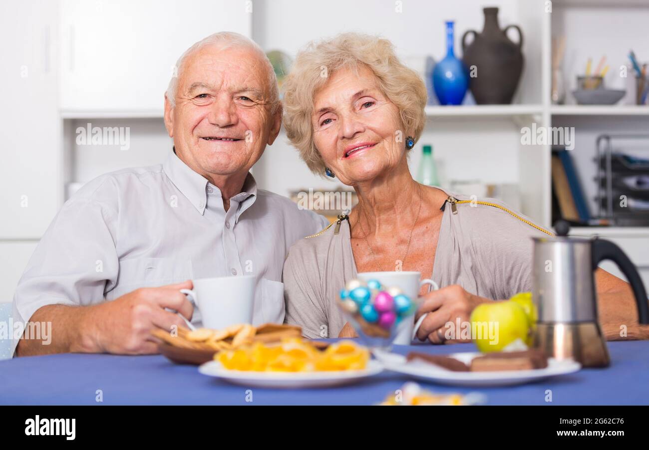 Smiling elderly spouses enjoying tea with sweets Stock Photo
