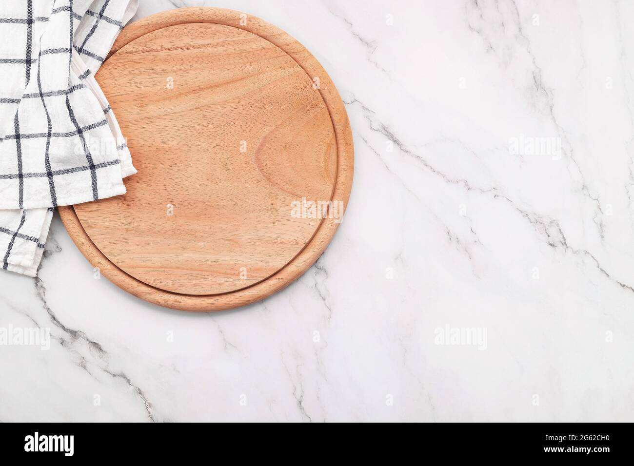 Empty wooden pizza platter with napkin and rolling pin set up on marble stone kitchen table. Stock Photo