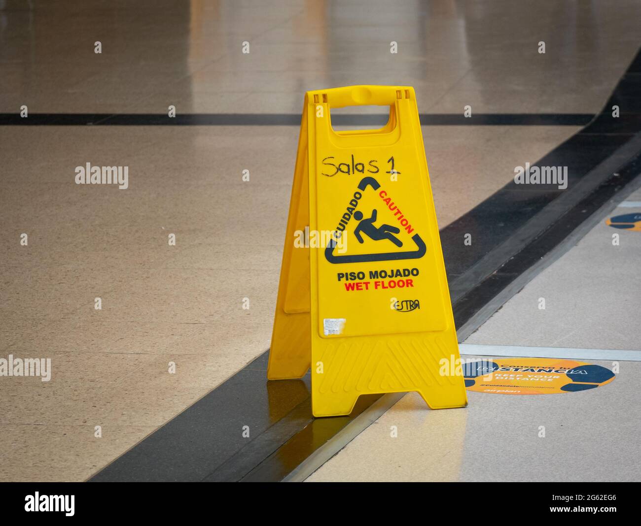 Yellow Wet Floor Warning Tool Written in English and Spanish at the Airport (Rooms 1 - Caution - Wet Floor -  Keep your Distance) Stock Photo