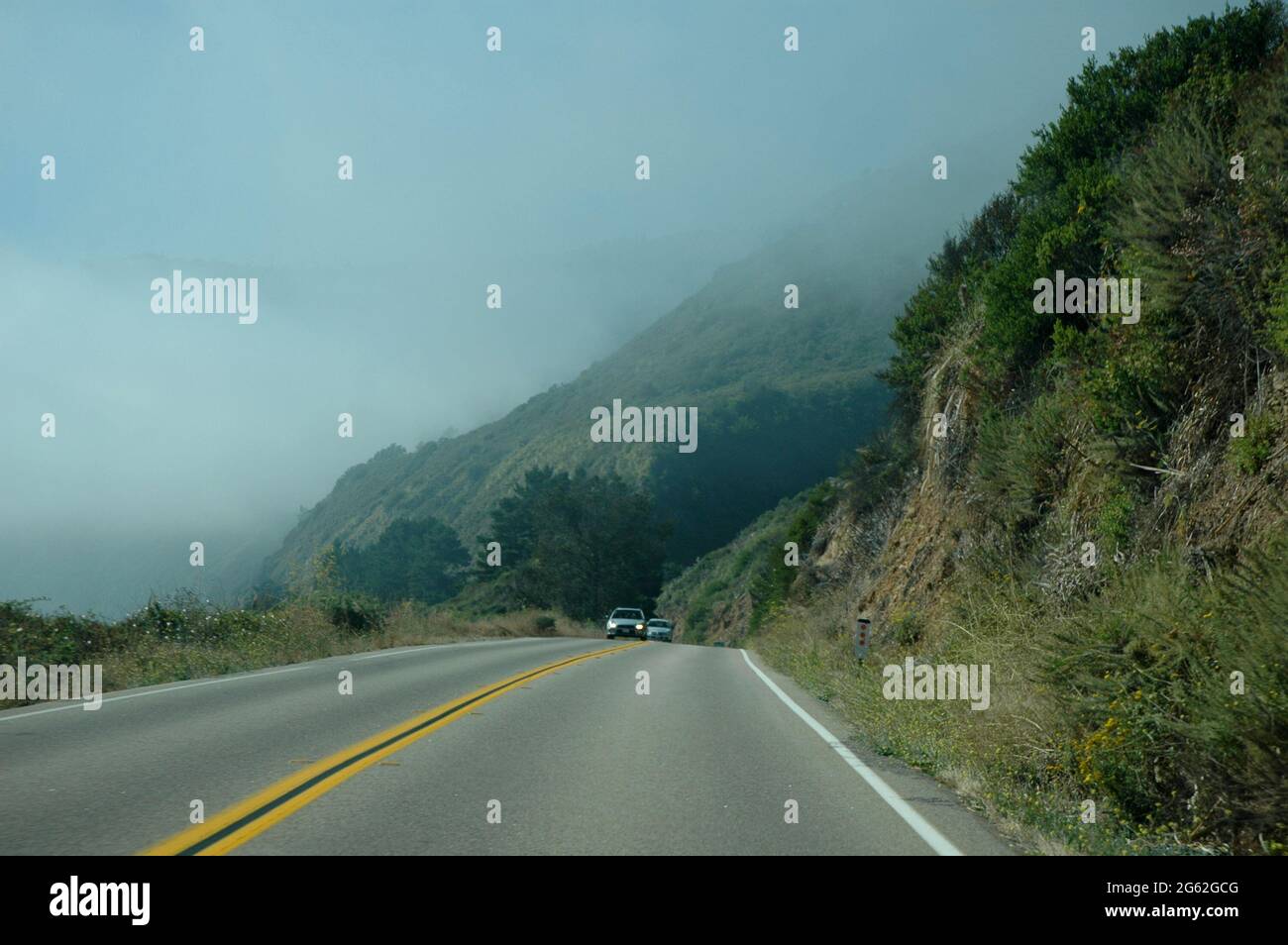 Driving North on Pacific Coast Highway in California on sunny afternoon with coastal fog and steep cliffs Stock Photo