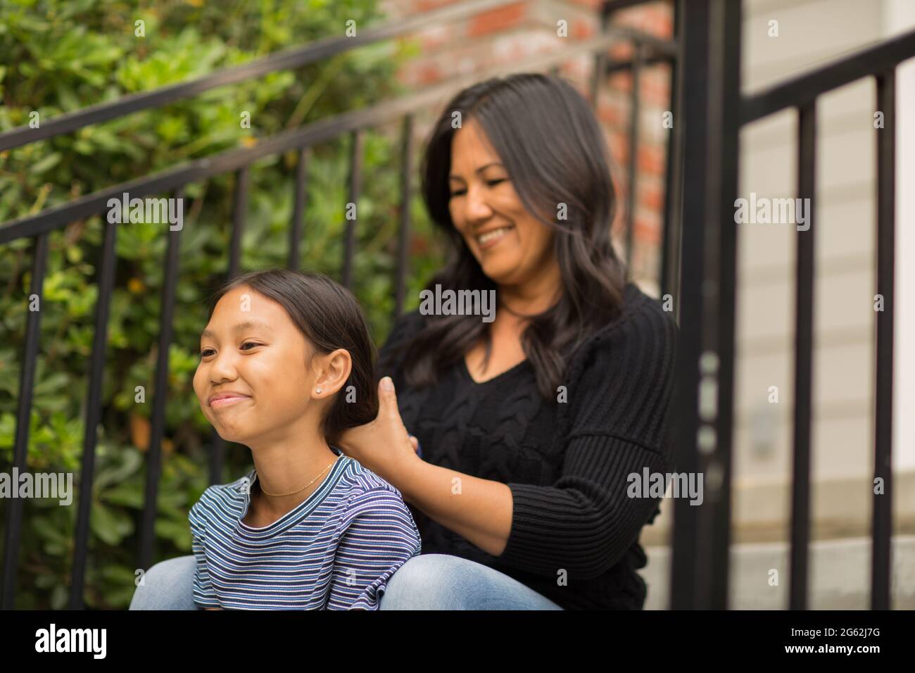 Asian mom smiling and combing her daughters hair. Stock Photo