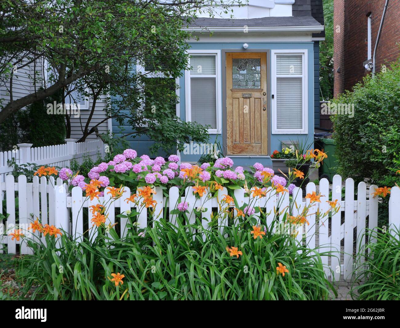 Charming small old house with white picket fence and flowers in front garden Stock Photo