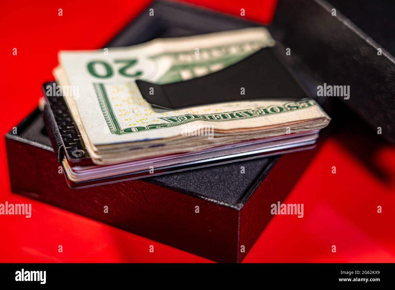 Selective focus of US dollar bills and credit cards in a black carbon fiber money clip placed on a black box. Red background. Stock Photo